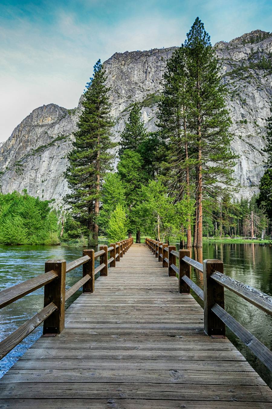 A wooden footbridge crossing the Merced River toward granite cliffs